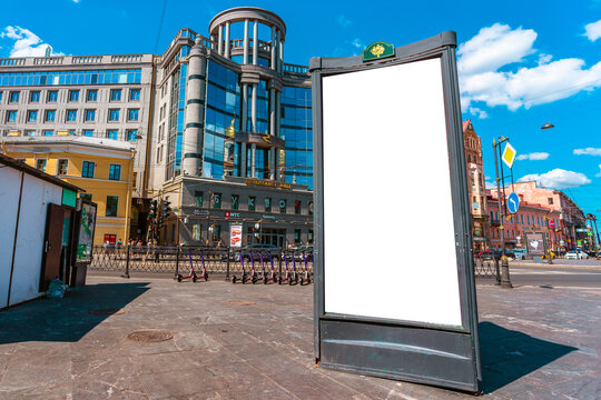 A vertical empty white billboard on a city street. A poster on the street next to the roadway. Saint Petersburg, Russia - 4 July 2021