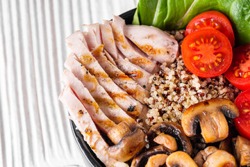 bowl of healthy quinoa with grilled chicken and vegetables on a white rustic wooden background