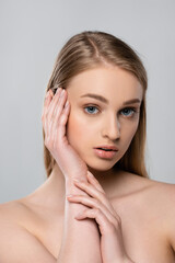 young woman with bare shoulders touching face isolated on grey