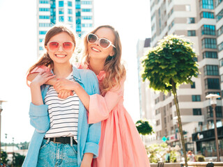Two young beautiful smiling hipster female in trendy summer clothes and dress.Sexy carefree women posing on the street background. Positive pure models having fun at sunset, hugging and going crazy