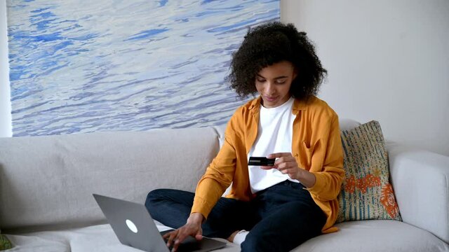 Online shopping. Young beautiful african american woman in casual stylish clothes sits on the couch, makes purchases via internet, fills in credit card details to pay for goods or home delivery