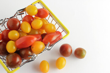 Fresh cherry tomatoes of different varieties in a souvenir commodity iron basket. Top view on a white background.