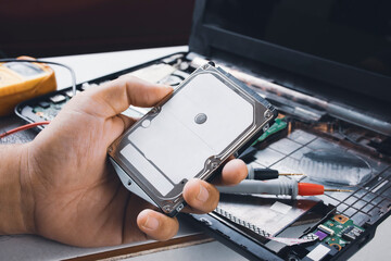 Hard disk drives 2.5 inch (HDD) holding on the mechanic hand with computer laptop and multimeter probe background