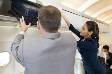 flight attendant helping passenger with carry on luggage to overhead bins