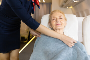 flight attendant or air hostess covering a blanket to senior woman passengers on airplane