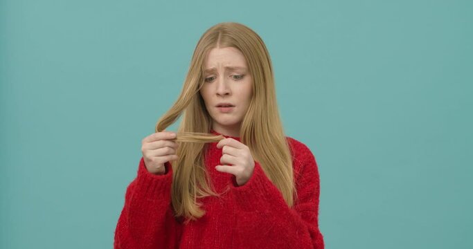 Young woman with long blond hair is upset and disappointed having split ends. Damaged hair
