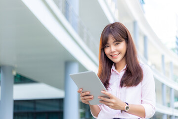 Fototapeta premium Happy young attractive business woman in her pink shirt using her tablet computer to check her social media outside of her office building