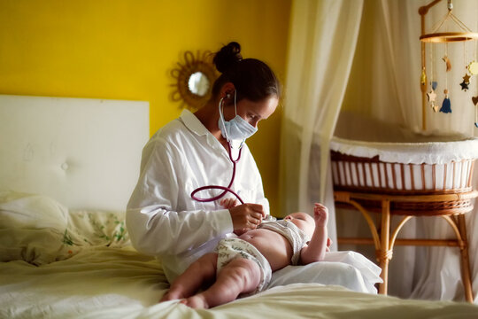 Doctor nurse listens with a stethoscope to baby child at home in bedroom, examination of baby at home, patronage. Regular medical check-ups for babies