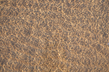 View through the water and waves on the sand with sunlight, abstract natural background