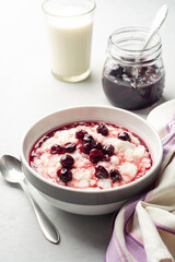 Rice pudding or porridge with cherry jam in bowl on concrete background