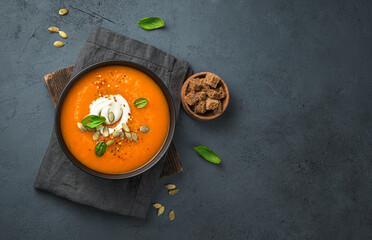 Pumpkin soup with cream and carrots on a dark gray background. Top view, copy space.