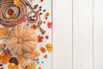 Festive autumn decor made of pumpkin and autumn leaves on a light wooden background.