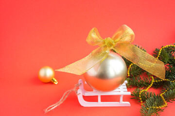Christmas composition with gold ball on a white toy sleigh on the red background