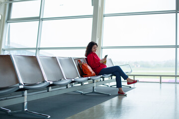 A girl is sitting on an empty row of seats in front of a large stained glass window in an airport...