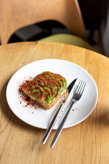Avocado toast on the whole wheat  bread with knife and fork on the white plate