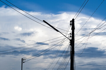 Electrical voltage pole with street lamp blue sky and white cloud silhouette.