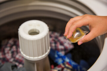 Child's Hand Placing Laundry Pod in Top Loading Washing Machine