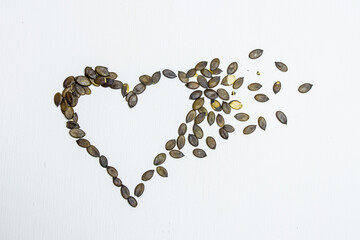 Natural pumpkin seeds in heart shape lying on a white wooden background