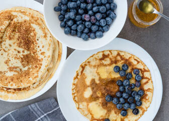 Pancakes, blueberries and honey on a white table on a gray concrete background. Maslenitsa concept and summer time. 
