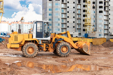 Obraz na płótnie Canvas Heavy wheel loader with a bucket at a construction site. Equipment for earthworks, transportation and loading of bulk materials - earth, sand, crushed stone.