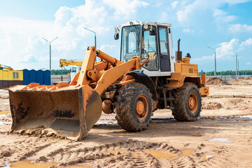Fototapeta premium Heavy wheel loader with a bucket at a construction site. Equipment for earthworks, transportation and loading of bulk materials - earth, sand, crushed stone.