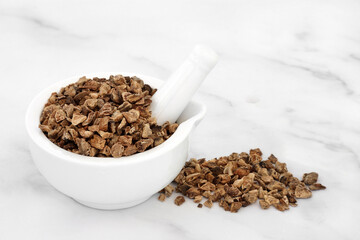 Devils claw root in a mortar with pestle used in herbal medicine to treat arteriosclerosis, arthritis, gout, fibromyalgia, tendonitis, heartburn, migraine, muscle pain and fever. On marble background.
