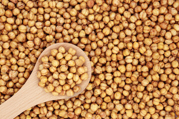 Spicy roasted organic chickpeas for a healthy snack in a wooden spoon and forming a background. High in fibre, protein, vitamins and minerals. Flat lay.