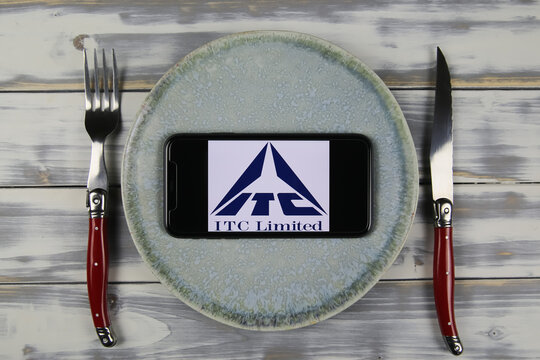 Viersen, Germany - May 9. 2021: Closeup of mobile phone on plate and wood table, cutlery with logo lettering of indian itc limited company (focus on center)