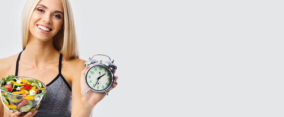 Woman with alarm clock and greece salad with vegetables and cheese, over grey background with copy...