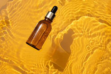 Amber glass dropper bottle with metallic lid on a light orange background. Mockup with cosmetic oil...