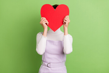 Photo of young girl close cover face big red paper heart card anonym incognito isolated over green color background