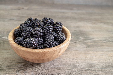 Fresh blackberries in a bamboo bowl on a wooden table close up. Healthy diet high in antioxidants and fresh fruit healthy eating concept.