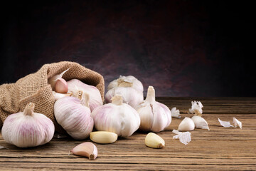 Garlic, packed in sacks, placed on an old wooden table in the kitchen on a dark black wall background.