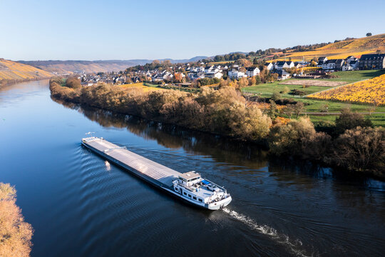 Germany, Rhineland-Palatinate, Helicopter view of barge sailing along Moselle river with village in background