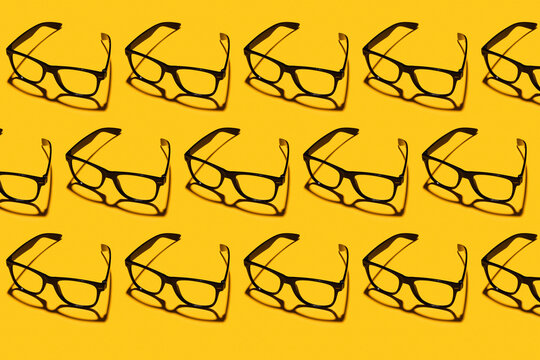 Pattern of rows of simple classic eyeglasses flat laid against yellow background