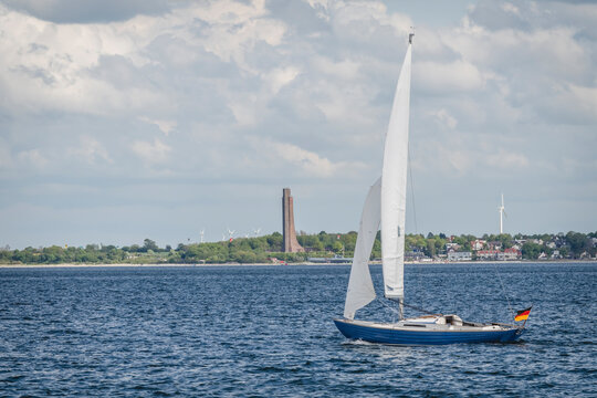 Germany, Schleswig-Holstein, Laboe, Lone sailboat sailing along Kiel Fjord with Laboe Naval Memorial in background