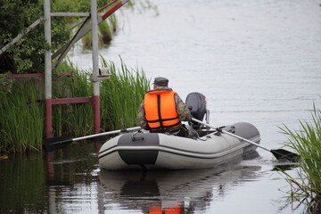 A fisher man in orange lifejacket paddles on an gray inflatable motor boat with broken outboard...