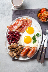 English Breakfast with fried eggs, sausages, bacon, beans, toasts, tomatoes and mushrooms on white plate, concrette background, Top view
