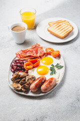 English Breakfast with fried eggs, sausages, bacon, beans, toasts, tomatoes and mushrooms on white plate, concrette background, Top view