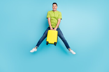 Full size photo of cheerful young positive man jump up air hold luggage enjoy isolated on blue color background