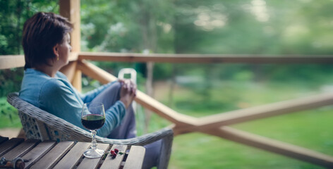 Lonely woman with a glass of wine looks into the garden on the veranda, depression and loneliness, banner