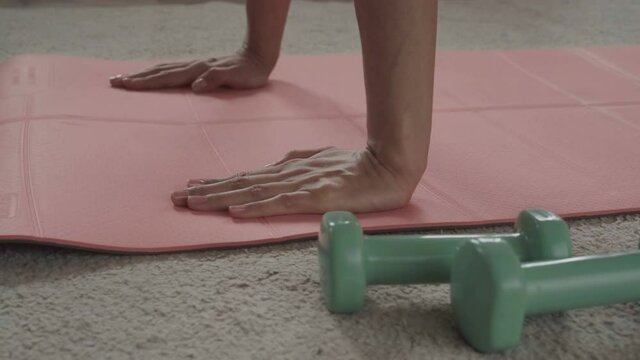 Closeup of female hands on a pink rug for yoga. Concept of domestic training. On the floor lie races and rope