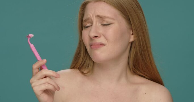 Naked young woman refuses to use razor isolated over blue background.