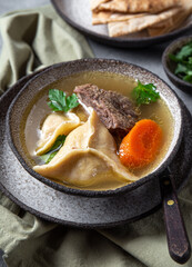Traditional Jewish food dumplingd kreplach soup in gray bowl.