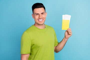 Photo of cheerful happy young man hold hands tickers passport smile isolated on blue color background