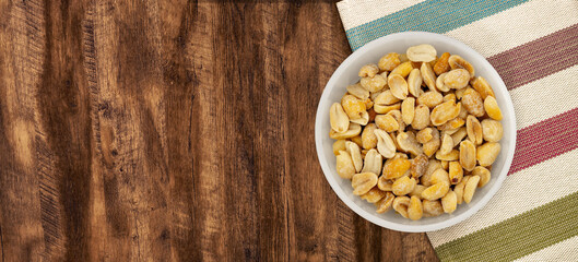 Salted peanuts in white bowl, photographed overhead on dark wood with natural light. Top view of bowl with salty peanut.