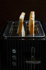 Toasted bread popping up from a black retro toaster, closeup view