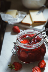 Homemade strawberry jam in a jar, fresh strawberries, bread and butter on kitchen table