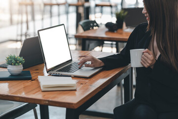 Side view of a businesswoman holding a coffee cup with using a laptop at her desk.