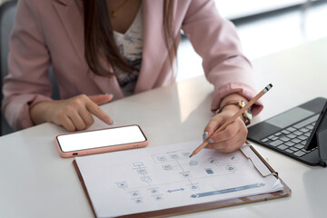 Image businesswoman holding a pencil with a smartphone blank white screen pointing at the graph at the office. Mock up.